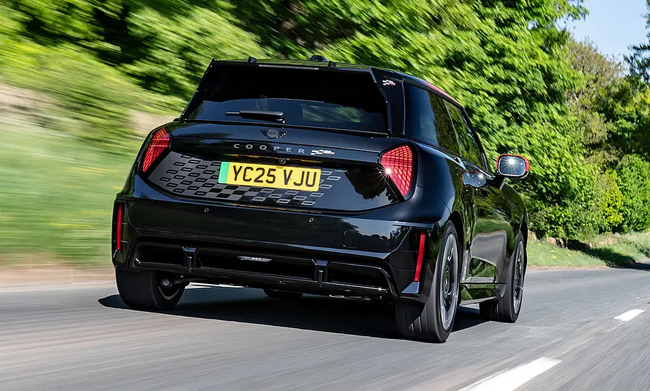 Der Mini JCW Electric (2025) fährt über eine Landstraße, fotografiert von schräg hinten.