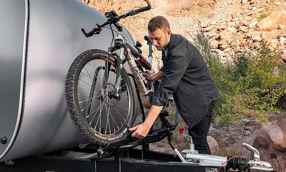 Das Bild zeigt den Deichselfahrradträger des Miniatouring M24 (2025). Eine Person fixiert ein Mountainbike auf dem Träger.