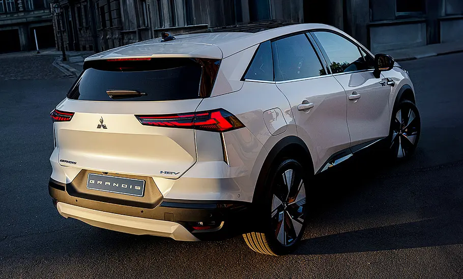 Der Mitsubishi Grandis (2025) fahrend von schräg hinten fotografiert vor einer städtischen Kulisse.