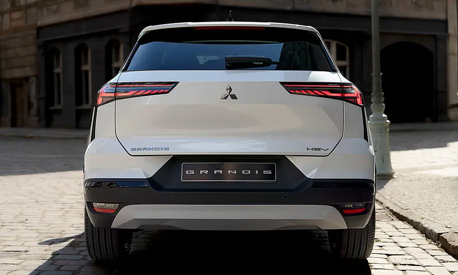 Der Mitsubishi Grandis (2025) fahrend von hinten fotografiert vor einer städtischen Kulisse.