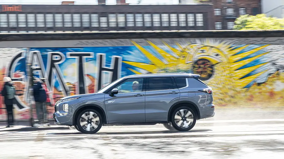 Mitsubishi Outlander fährt an der Berliner Mauer vorbei. Ansicht des Fahrzeugs von der linken Seite.