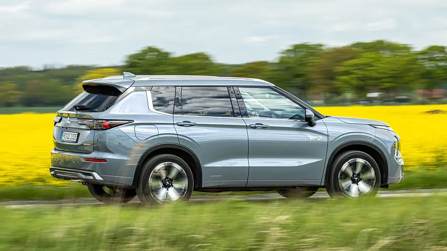 Mitsubishi Outlander fährt auf einer Landstraße, Ansicht von der linken Seite.