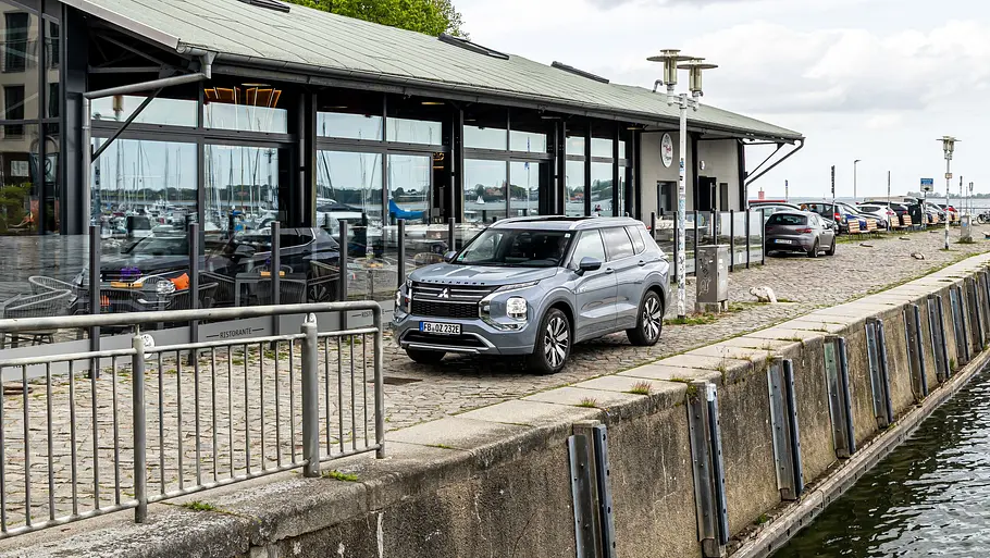Mitsubishi Outlander vor dem Ippen-Schuppen, im Vordergrund ein Gewässer.