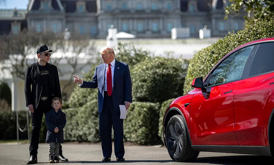 Elon Musk neben Donald Trump, im Bild sieht man auch einen Sohn von Elon Musk sowie im Vordergrund einen Tesla.