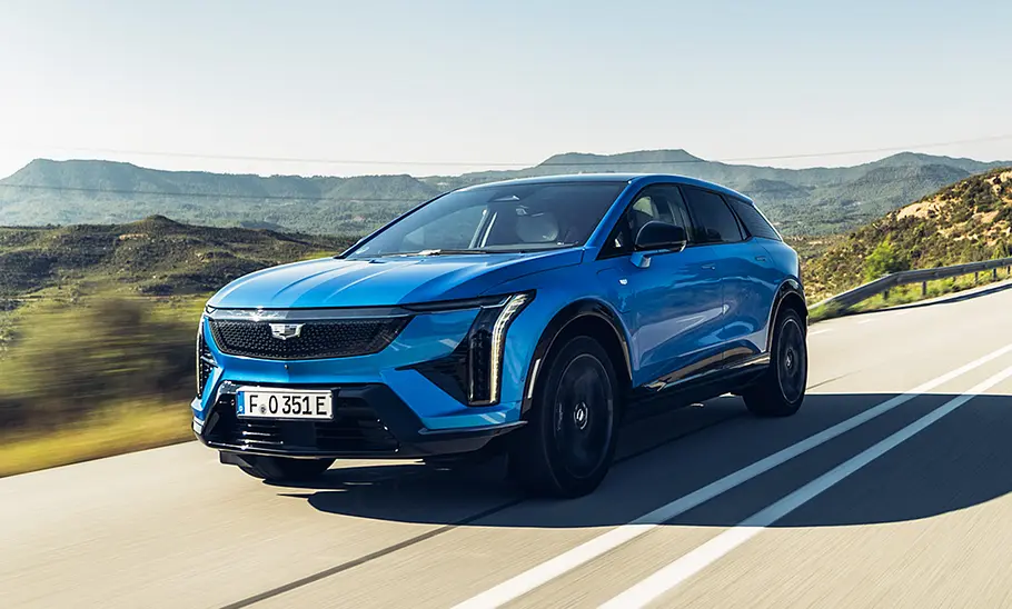 Der Cadillac Optiq (2026) fährt auf einer Straße. Fotografiert von vorne schräg.