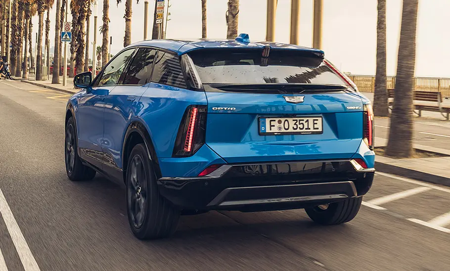 Der Cadillac Optiq (2026) fährt auf einer Straße am Strand. Fotografiert von hinten schräg.