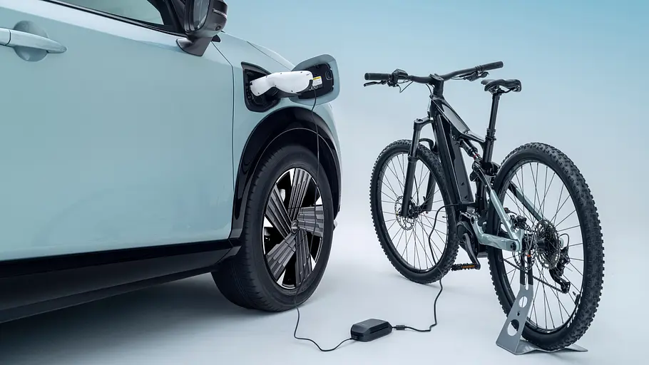 Ein E-Bike ist per Ladekabel über den Ladeanschluss mit dem Nissan Ariya Facelift (2026) verbunden.