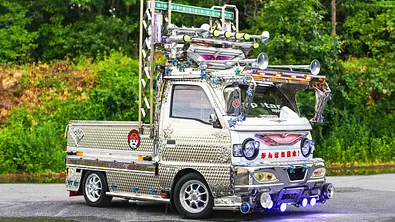 Der Suzuki Carry Dekotora steht vor einem Wald, fotografiert von schräg vorne. - Foto: Japstarz Imports
