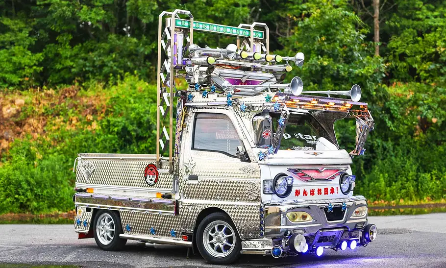 Der Suzuki Carry Dekotora steht vor einem Wald, fotografiert von schräg vorne.