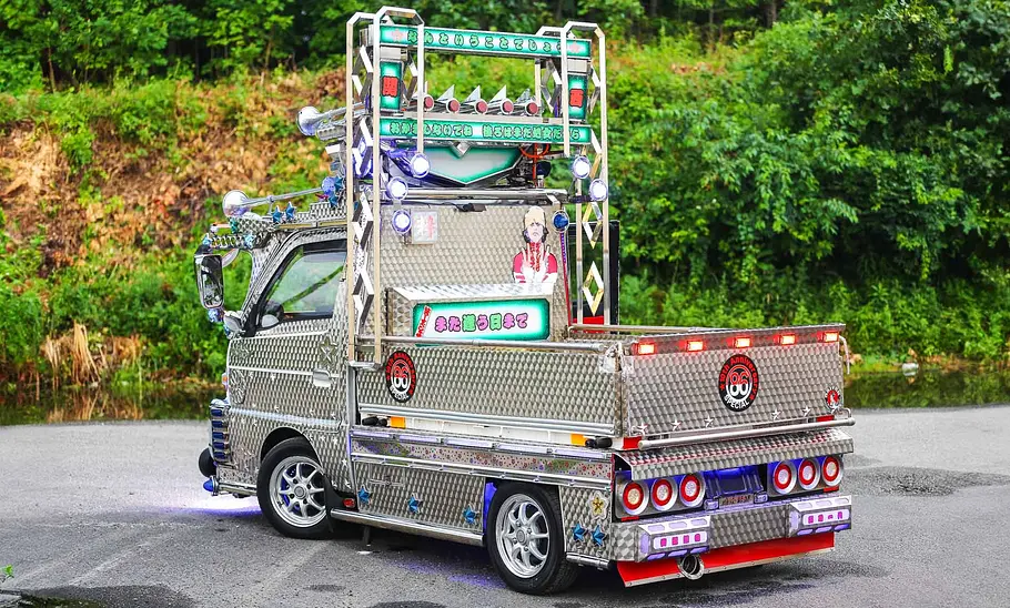 Der Suzuki Carry Dekotora steht vor einem Wald, fotografiert von schräg hinten.