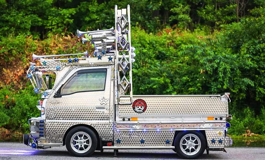 Der Suzuki Carry Dekotora steht vor einem Wald, seitlich fotografiert.