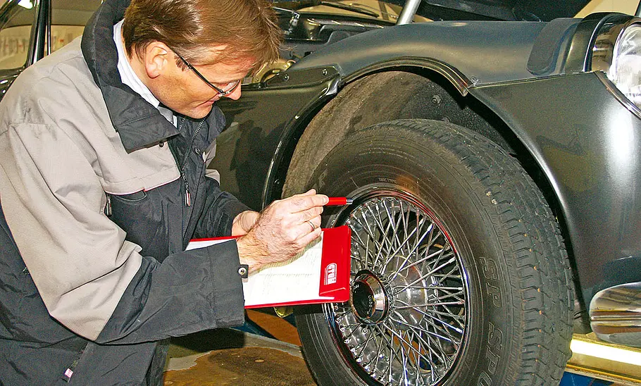 Ein Oldtimer-Gutachter prüft einen Oldtimer-Reifen und macht sich Notizen.