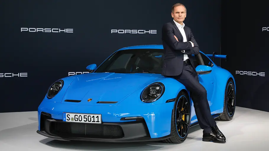 Oliver Blume Oliver Blume lehnt an einem Porsche, im Hintergrund sieht man den Porsche-Schriftzug.