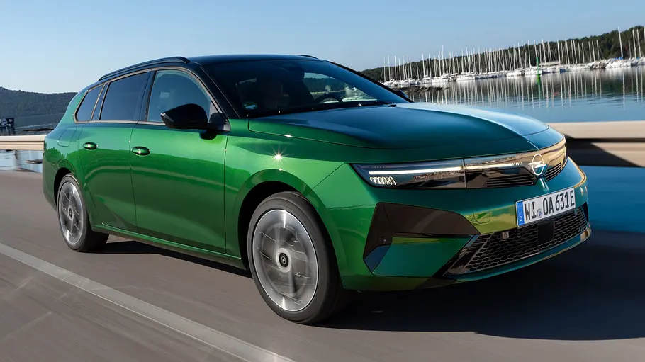 Der Opel Astra Sports Tourer fährt am Yachthafen entlang in der Farbe Klover Grün, fotografiert von vorne rechts.