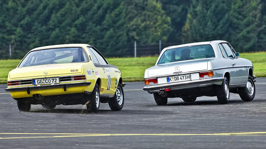Opel Commodore GS/E/Mercedes 280 CE fahrend von schräg hinten fotografiert. 