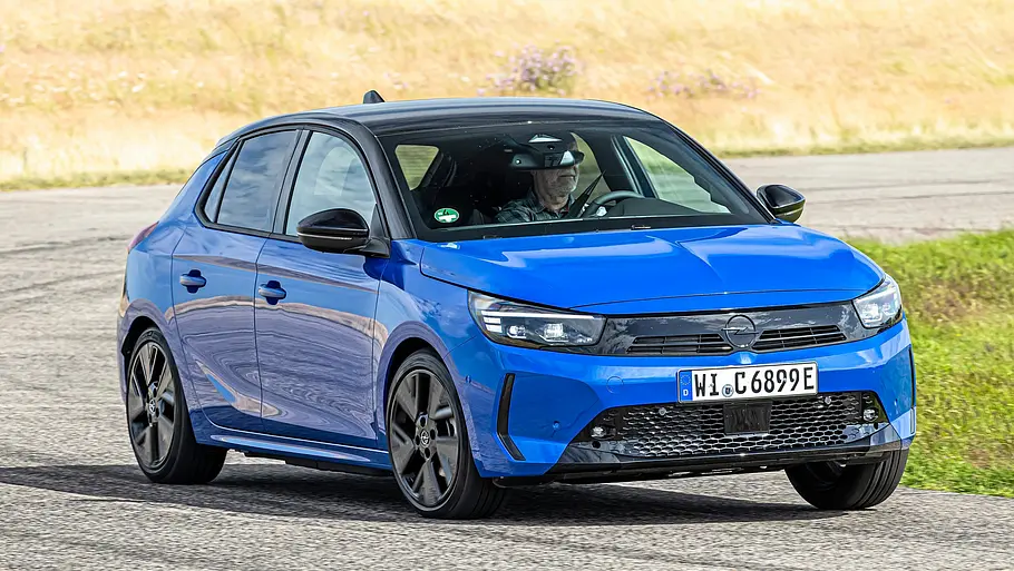Blauer Opel Corsa-e mit schwarzem Dach fährt auf dem Testgelände durch eine Kurve