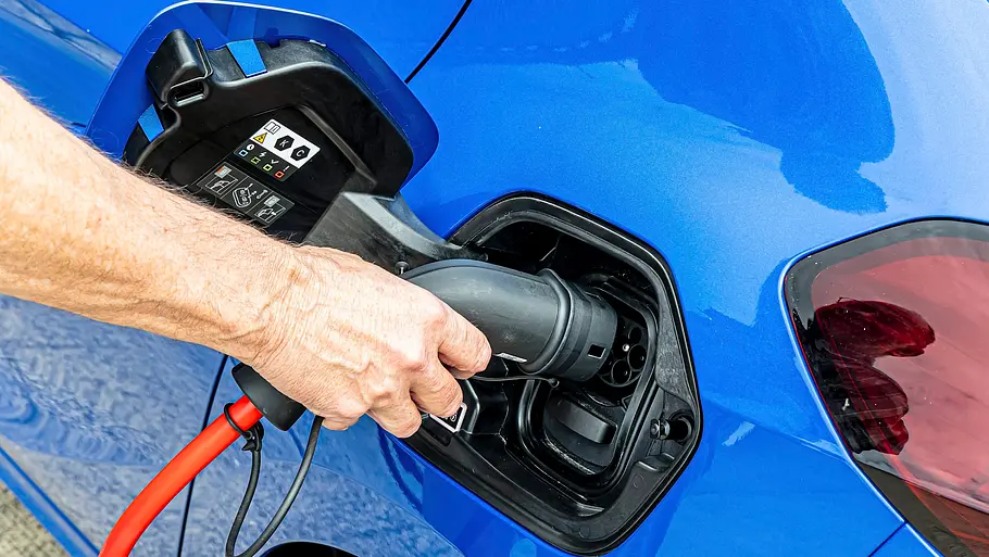 Hand steckt ein Ladekabel in den Ladeanschluss des blauen Opel Corsa-e