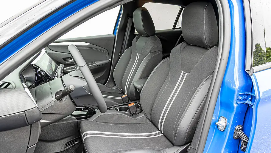 Blick durch die geöffnete Fahrertür auf die dunklen Vordersitze des Opel Corsa-e mit hellen Ziernähten