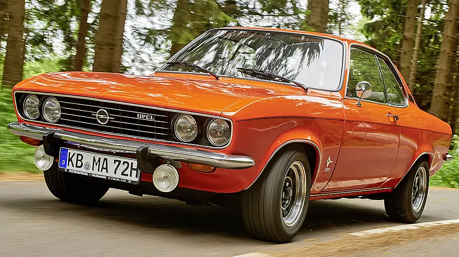Der Opel Manta A fährt auf einer Landstraße, von vorne links fotografiert.