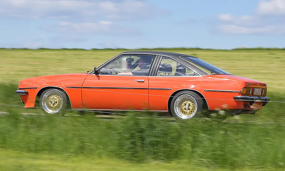 Der Opel Manta B 1.9 E fährt über eine Landstraße, von der Seite fotografiert.