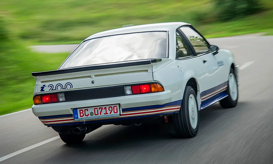 Der Opel Manta B i 200 fährt auf einer Straße, fotografiert von hinten schräg.