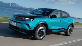 Der Opel Mokka Electric entlang einer Küstenlinie fahrend von schräg vorne links. - Foto: Opel