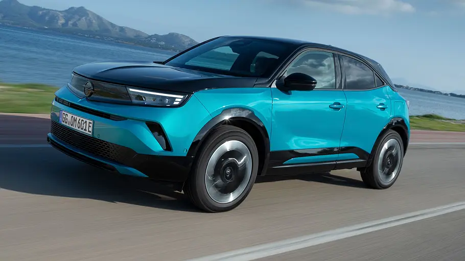Opel Mokka Electric Leasing-News Der Opel Mokka Electric entlang einer Küstenlinie fahrend von schräg vorne links.