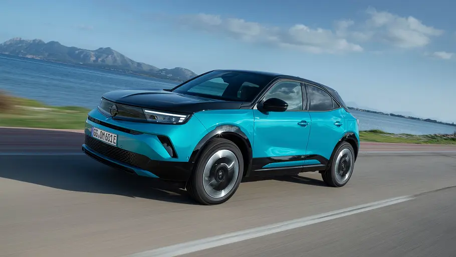 Opel Mokka Electric Leasing-News Der Opel Mokka Electric entlang einer Küstenlinie fahrend von schräg vorne links.