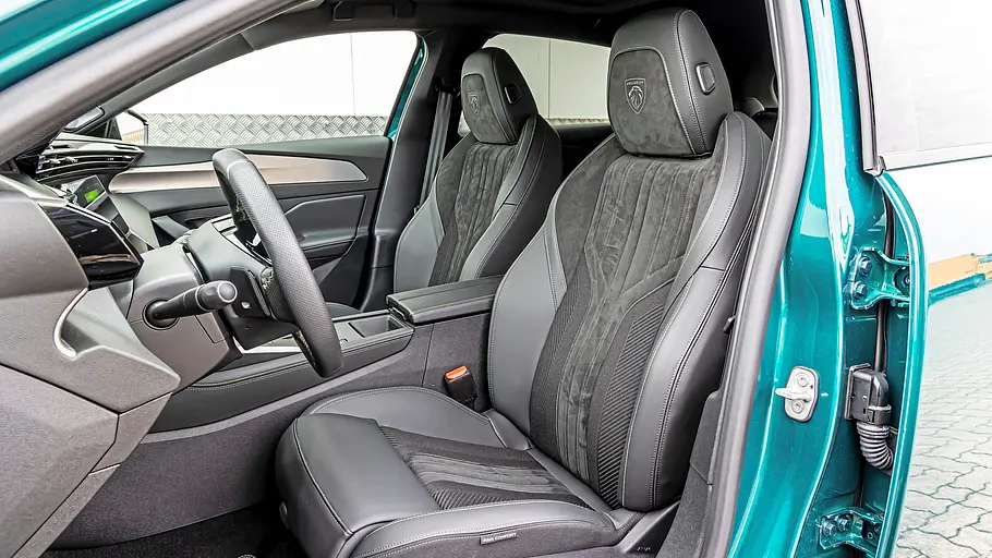 Durch die offene Fahrertür eines türkisfarbenen Peugeot 308 sind zwei schwarze Vordersitze, Lenkrad und Mittelkonsole zu sehen.