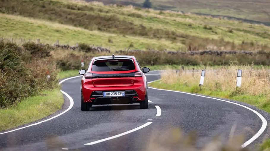 Peugeot E-208 GTi Fahrbericht Ein roter Peugeot E-208 GTi fährt auf einer asphaltierten, kurvigen Straße durch eine karge Berglandschaft.