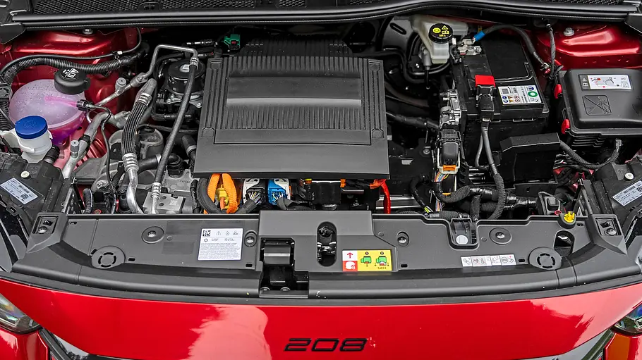 Peugeot E-208 GTi Fahrbericht Der geöffnete Motorraum eines roten Peugeot E-208 GTi zeigt eine schwarze Abdeckung, orange Kabel, eine Batterie und Flüssigkeitsbehälter.