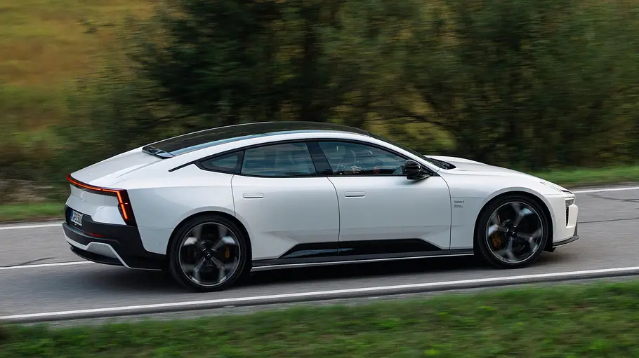Ein Polestar 5 Performance mit Panorama-Glasdach fährt auf einer Landstraße, umgeben von Wiesen und Bäumen.