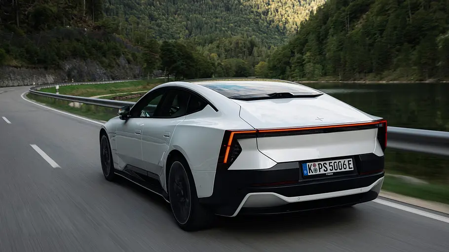 Ein Polestar 5 Performance mit Panorama-Glasdach fährt auf einer Landstraße, umgeben von Wiesen und Bäumen.