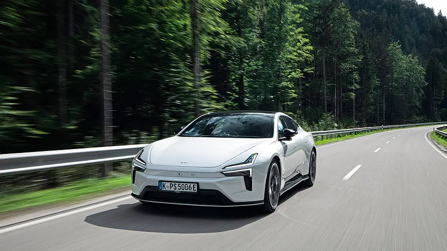 Ein Polestar 5 Performance mit Panorama-Glasdach fährt auf einer Landstraße, umgeben von Wiesen und Bäumen.