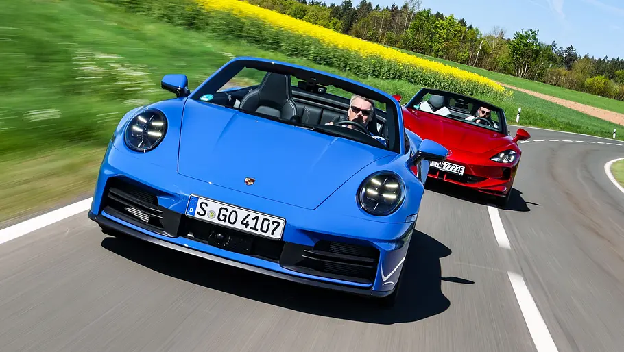 Das Porsche 911 Cabrio und der MG Cyberster fahren hintereinander über einer Landstraße, fotografiert von vorne.
