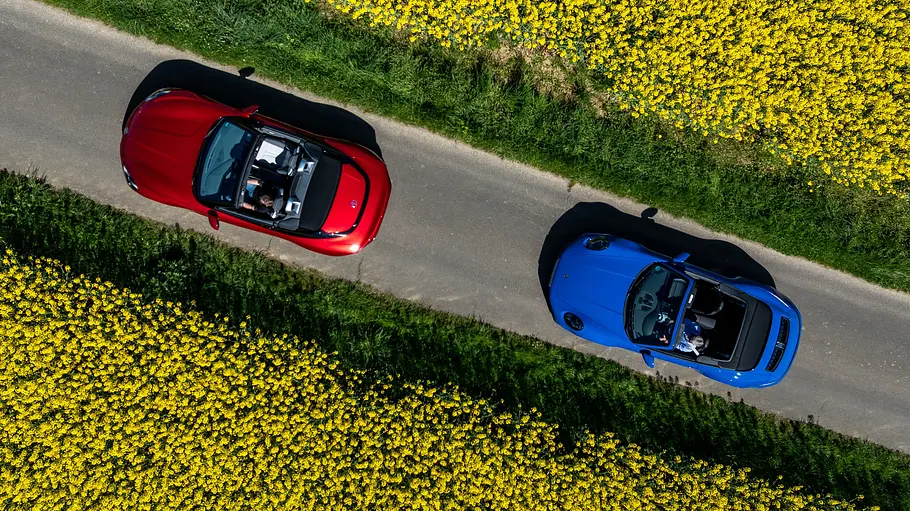 Der MG Cyberster und das Porsche 911 Cabrio fahren hintereinander über einer Landstraße, fotografiert von oben.