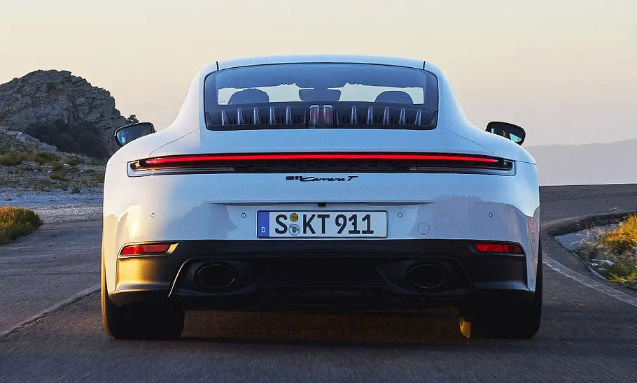 Der Porsche 911 Carrera T (2024) fährt auf einer Straße entlang; Blick von hinten auf das Auto.