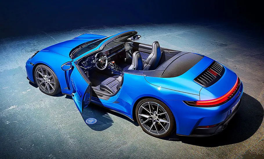 Das blaue Porsche 911 Carrera T Cabrio (2024) steht in einer dunklen Umgebung. Blick von schräg hinten auf das Auto.