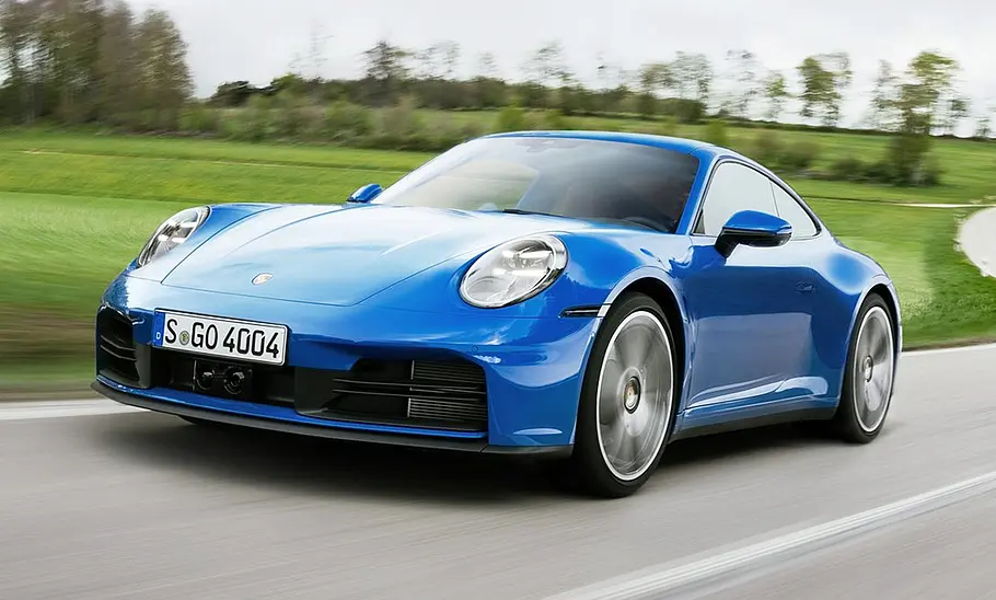 Blick von vorne auf das Porsche 911 Carrera Facelift (2024), das auf einer Landstraße entlang fährt.
