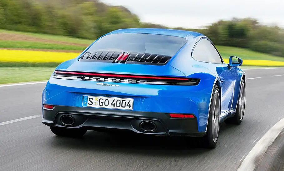 Blick von hinten auf das Porsche 911 Carrera Facelift (2024), das auf einer Landstraße entlang fährt.