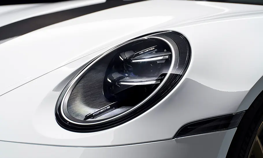 Porsche 911 (992) GT3 Facelift (2024): Weißer Sportwagen steht vor dunklem Hintergrund. Detailanblick auf die Scheinwerfer.