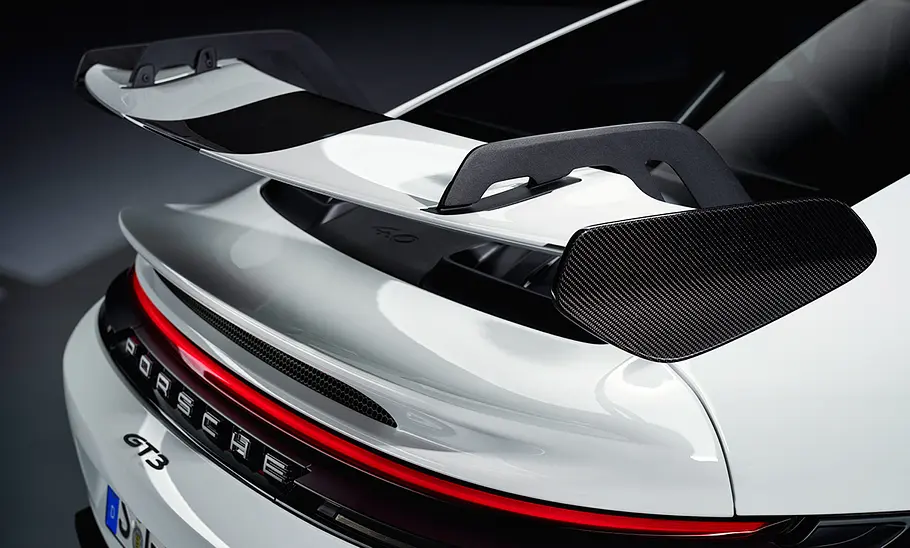 Porsche 911 (992) GT3 Facelift (2024): Weißer Sportwagen steht vor dunklem Hintergrund. Detailanblick auf den Heckflügel.