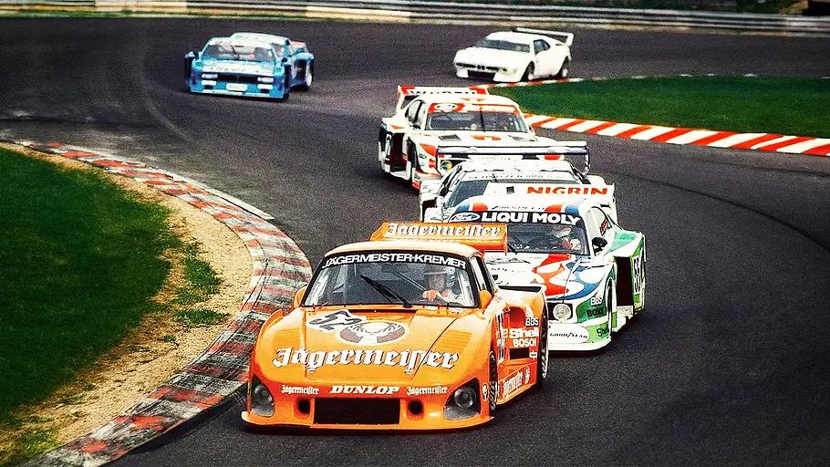 Blick von vorne auf den Porsche 935 Kremer und weitere Rennautos, die eine Kurve passieren.