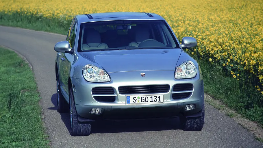 Der Porsche Cayenne fährt auf einer kleinen Straße neben einem Rapsfeld, von vorne fotografiert.