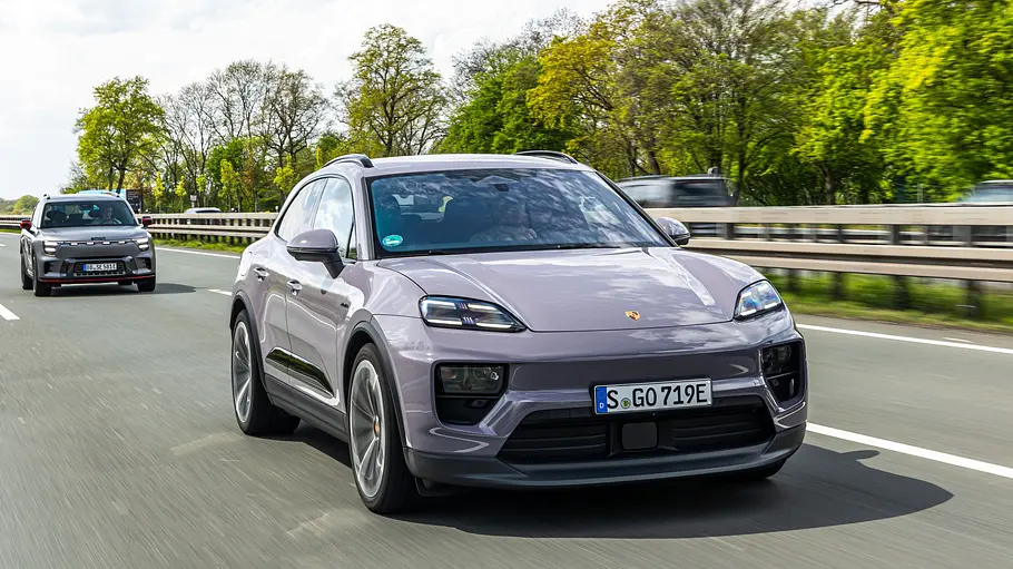 Ein hellvioletter Porsche Macan fährt auf einer Autobahn. Dahinter folgen weitere Autos, am Straßenrand stehen grüne Bäume.