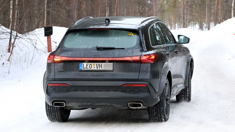 Der Porsche Octan fährt als Mule mir der Karosserie es Audi Q5 auf einer Landstraße, von hinten fotografiert.