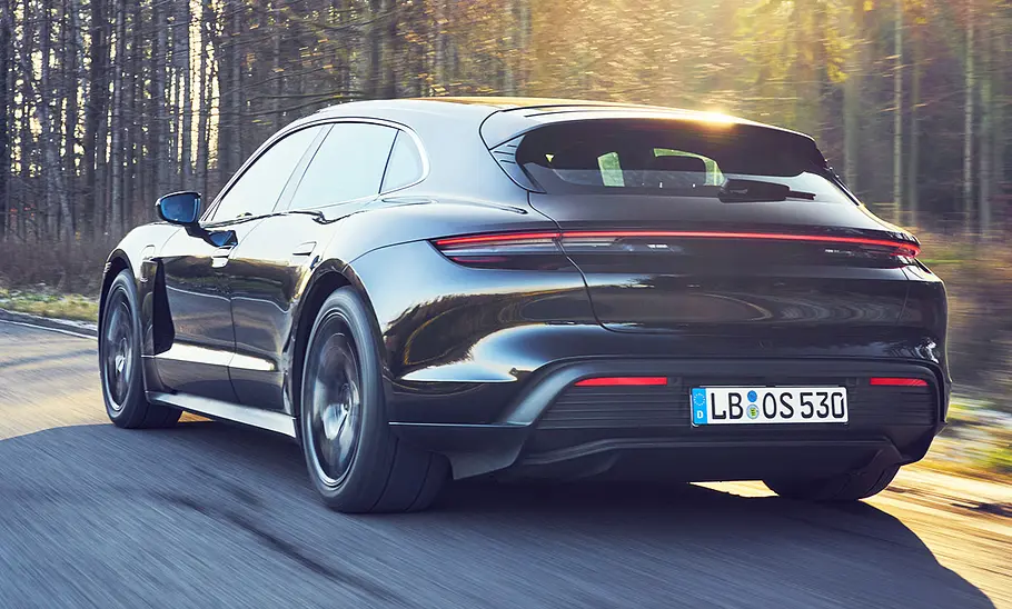 Das Porsche Taycan Turbo S Sport Turismo Facelift (2024) fährt über eine Landstraße, von schräg hinten fotografiert.