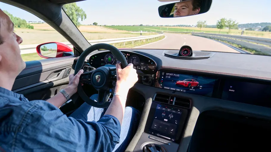 Porsche Taycan GTS Cockpit, eine Person sitzt am Steuer und fährt über eine Straße.