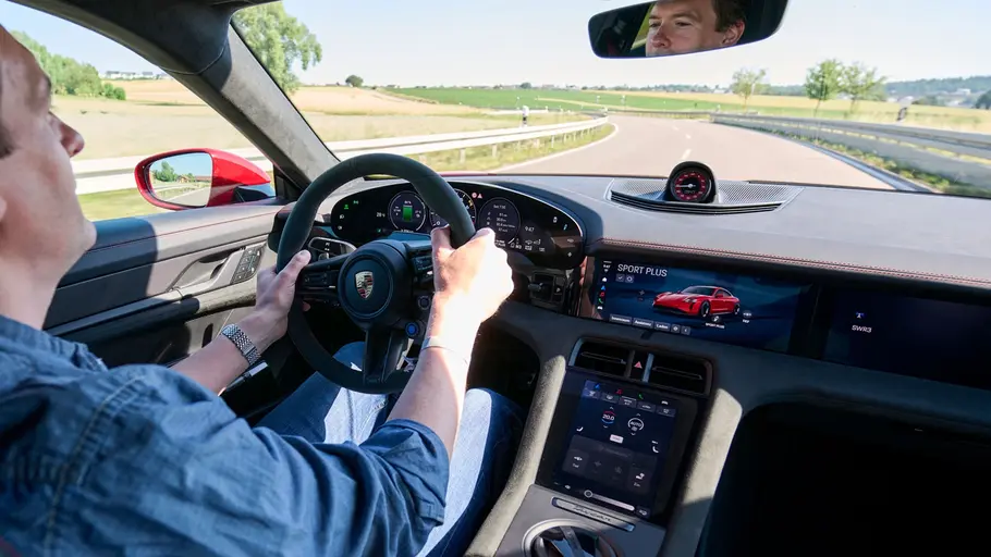 Porsche Taycan GTS Cockpit, eine Person sitzt am Steuer und fährt über eine Straße.