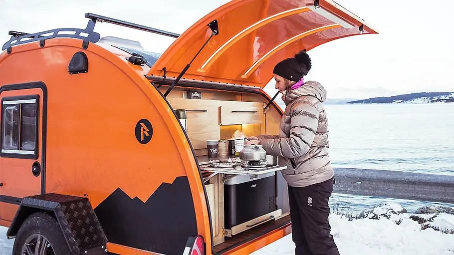 Das Foto zeigt eine Frau beim Kochen in der Heckküche des Raidhoo Tundra (2024) in winterlicher Landschaft.